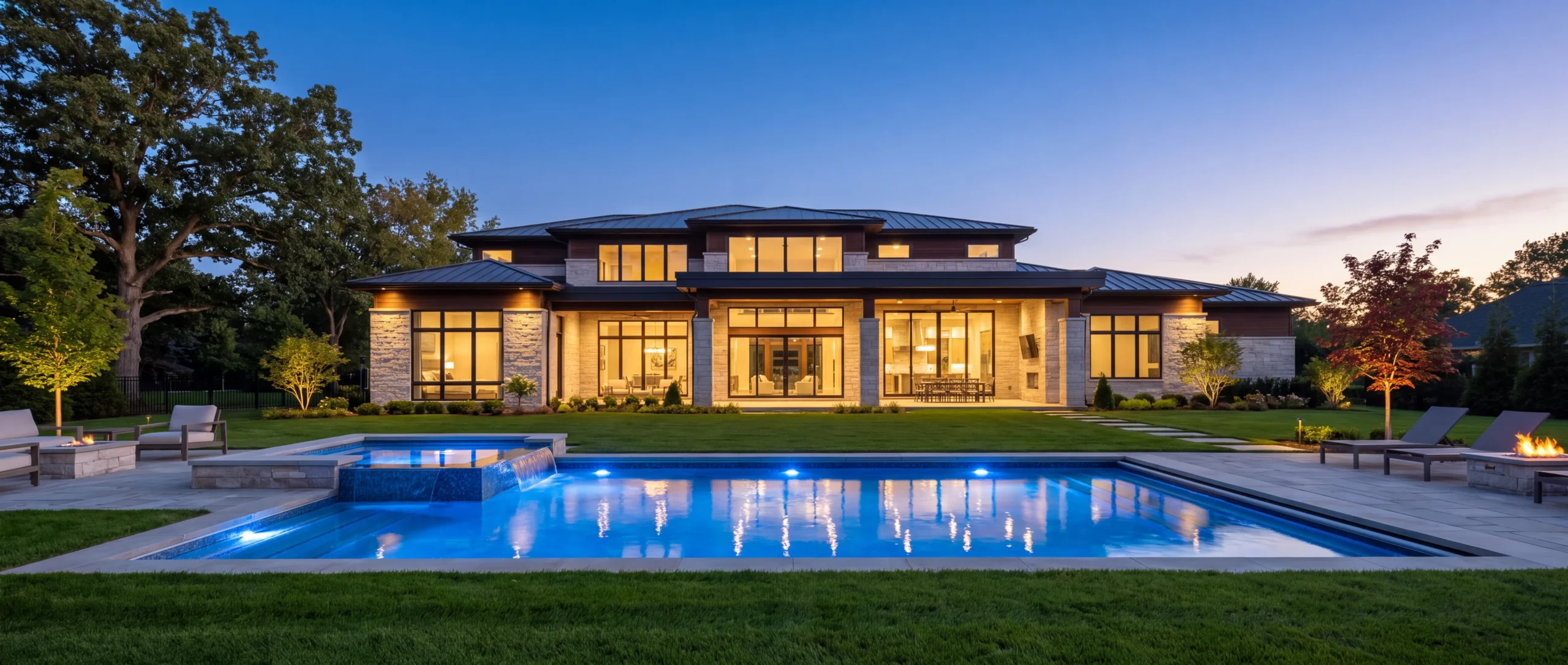 Newly built custom estate home at dusk with a blue-lit pool