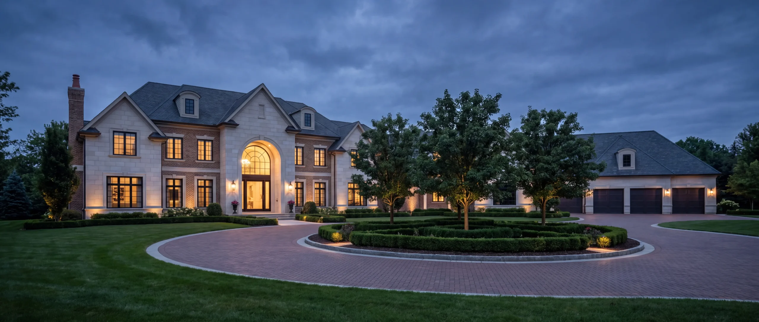 Front elevation of a newly built custom estate home at twilight with a circular paver motor court in Bloomfield Hills, Michigan